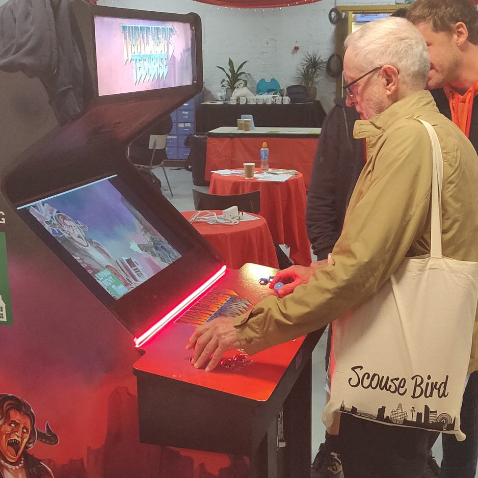 Jeremy Corbyn playing a thatcher game and wearing a scouse bird tote